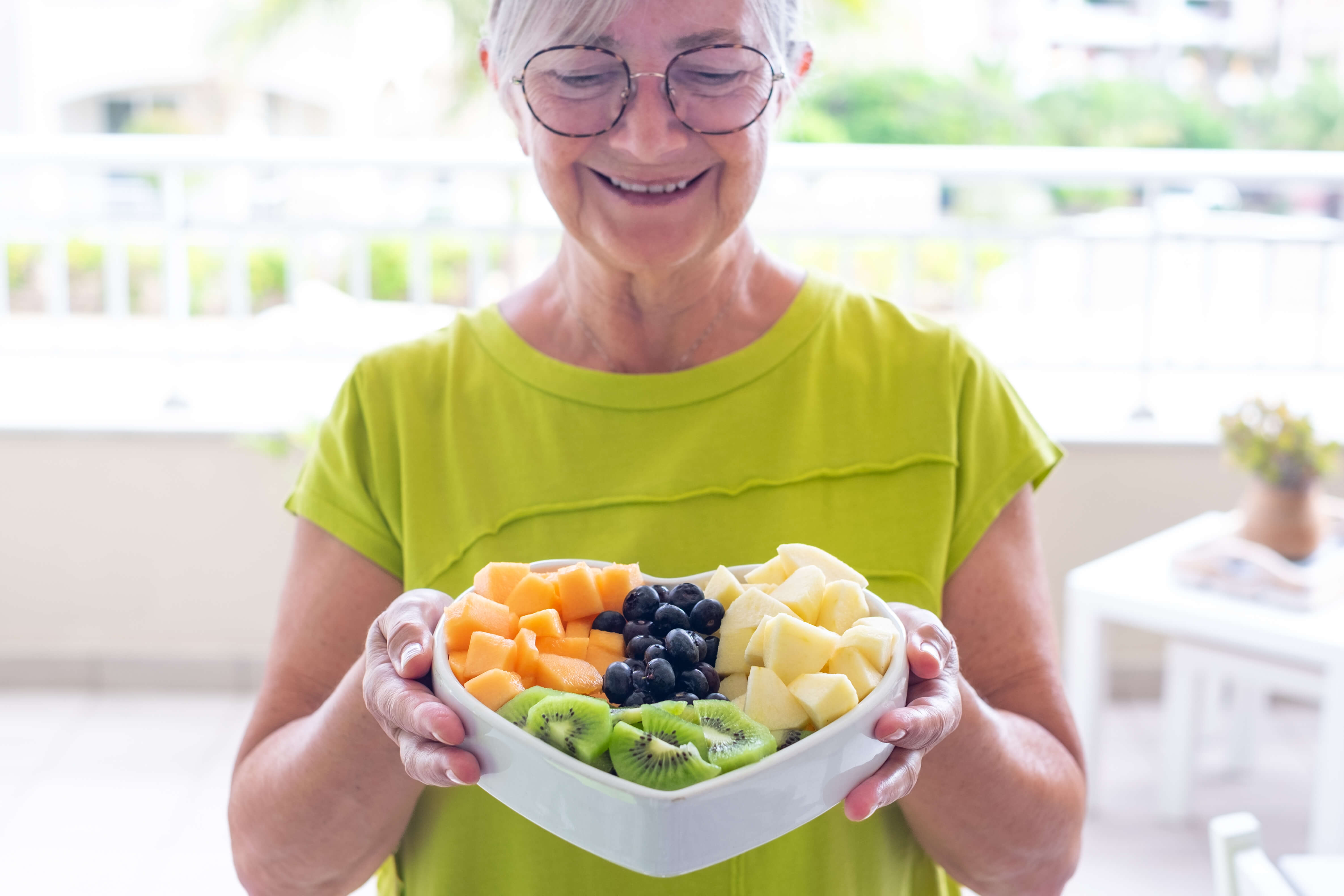 Senior lady smiling whilst holding a bowl of fruit
