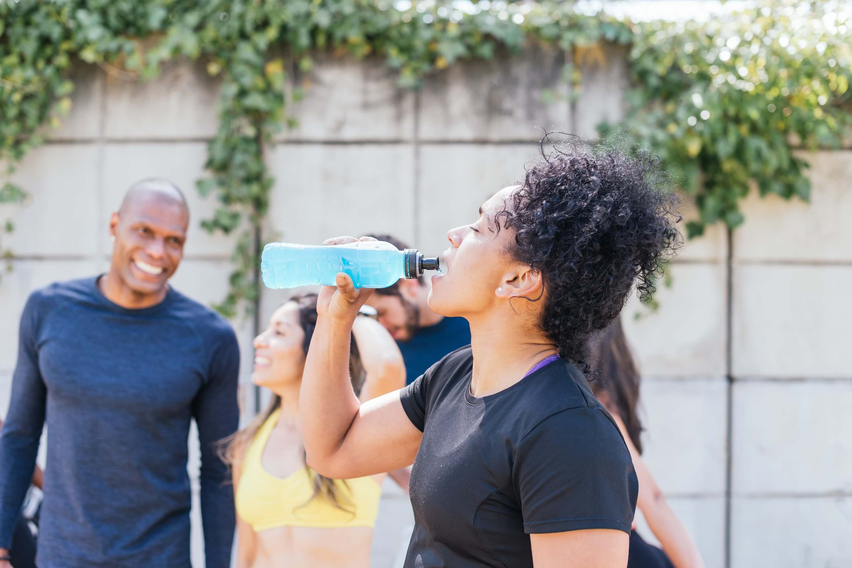 A lady drinking water surrounding by people after exercising