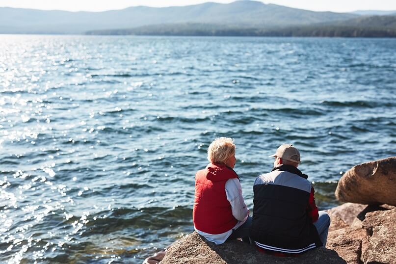 rear view of senior couple sat on the beach looking